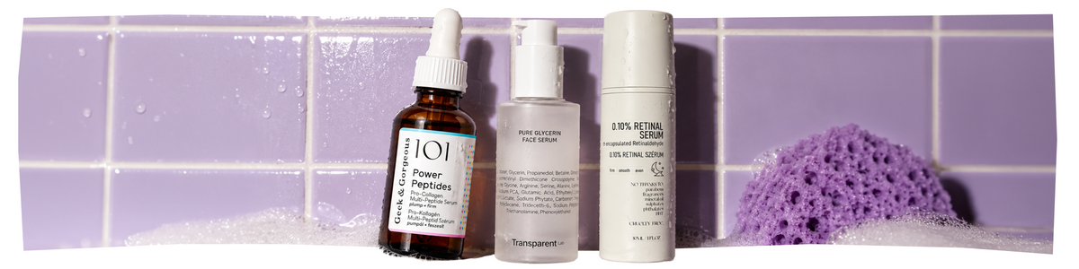 Drei Hautpflegeflaschen – Geek & Gorgeous Power Peptides, Transparent Lab Pure Glycerin Face Serum und ein 0,10-prozentiges Retinal-Serum – stehen vor einer lila gefliesten Wand, auf der ein lila Schwamm und Seifenblasen zu sehen sind.