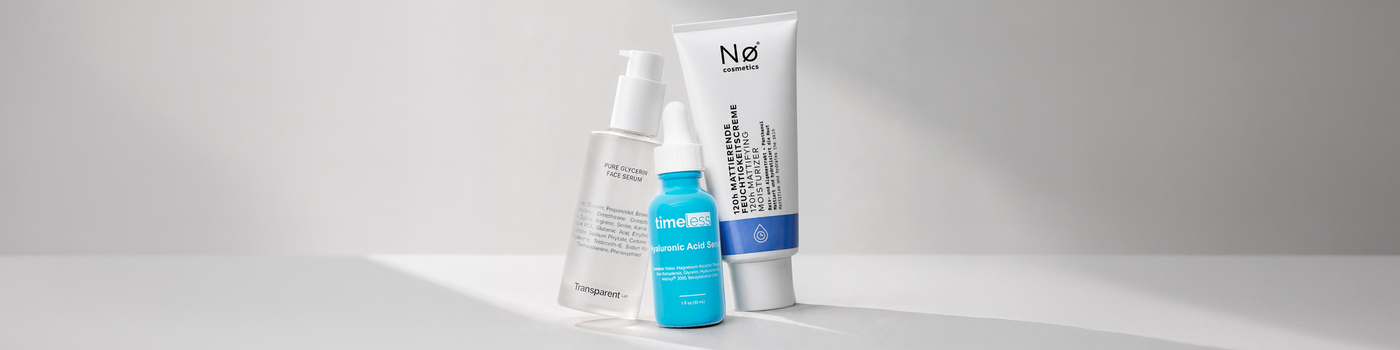 Drei Hautpflegeprodukte in klaren, blauen und weißen Flaschen auf einer weißen Fläche mit einem weichen Schatten.