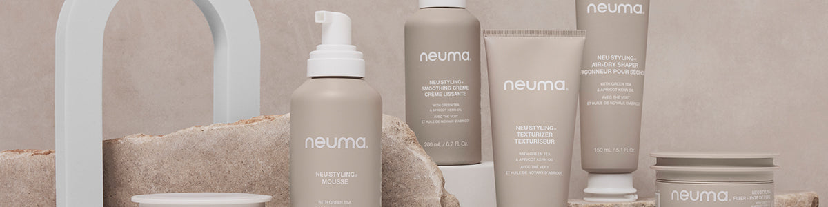 Neuma-Haarprodukte in beigen Flaschen, präsentiert auf Stein- und Bogenstützen vor einem sanften beigen Hintergrund.