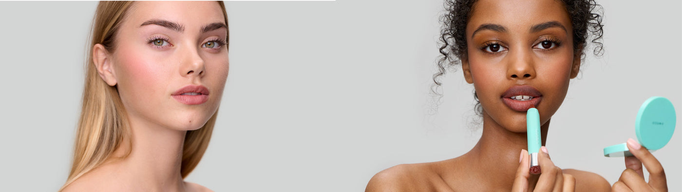 Zwei Frauen posieren vor einem hellgrauen Hintergrund. Die eine blickt in die Kamera, während die andere sich Lippenstift aufträgt und einen dazu passenden runden Spiegel in der Hand hält. Beide Models sind natürlich geschminkt.