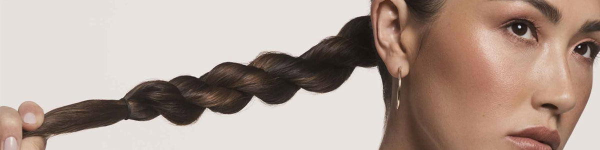 Eine Frau mit glatter Haut trägt ihr dunkles Haar zu einem ordentlichen Zopf geflochten und trägt einen kleinen Ohrring.