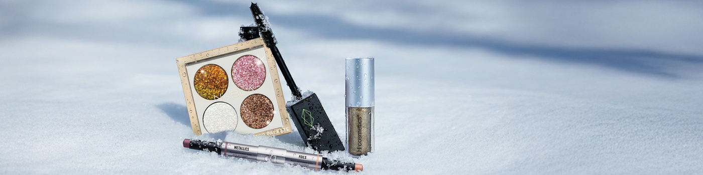 Glitzernde Make-up-Produkte, darunter eine Palette und Mascara, die auf frischem, weißem Schnee präsentiert werden.