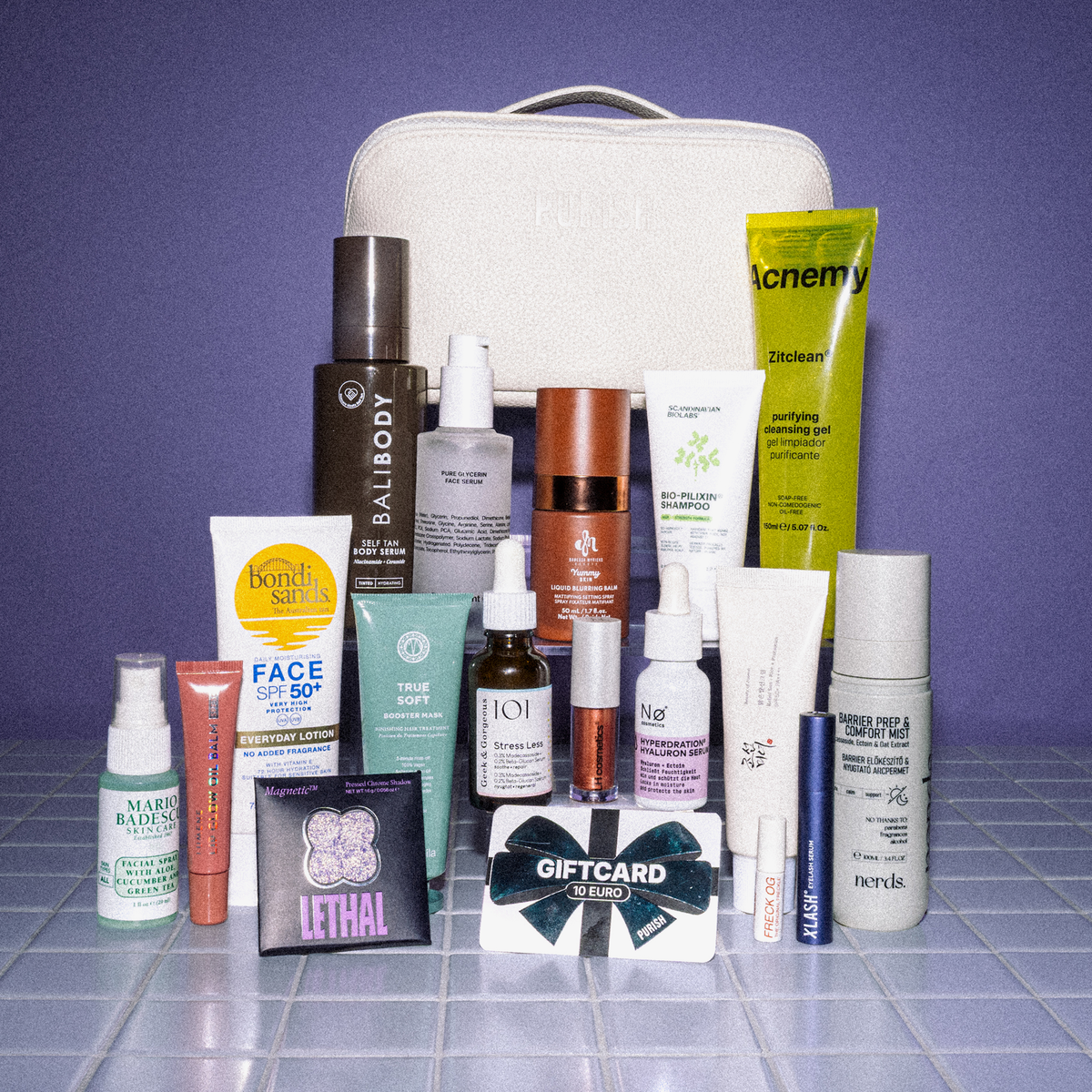 PURISH Favorites-Tasche mit Hautpflege- und Beauty-Essentials, angeordnet vor einem weißen Reißverschlussbeutel auf blauen Fliesen.