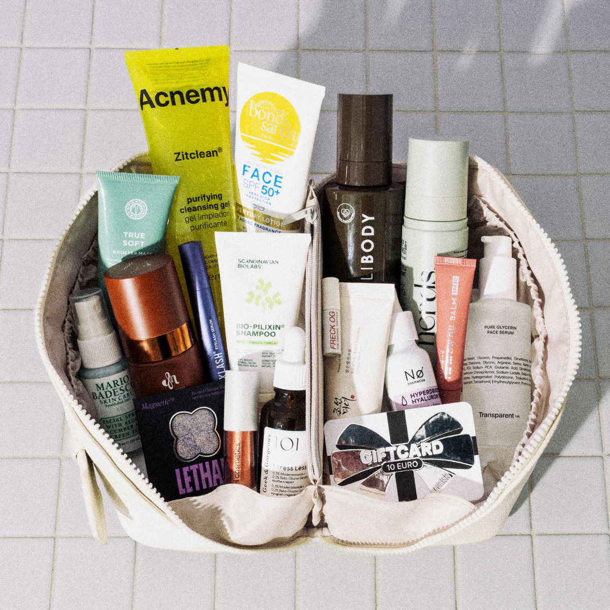 Offene „Purish Favorites“-Tasche von PURISH auf Fliesen, gefüllt mit Beauty-Produkten und einem gut sichtbaren 10-Euro-Geschenkgutschein.