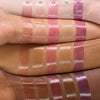 Swatches von fünf glänzenden Lipgloss-Sticks (010–050) auf Armen mit unterschiedlichen Hauttönen, um die Farbwirkung der Produkte zu zeigen.