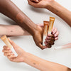 Mehrere Hände mit Catrice Under Eye Brightener, Farbtöne 010, 020, 030 und 040 sind auf unterschiedlichen Hauttönen als Swatches zu sehen.