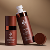 Zwei braune Flaschen Danessa Myricks Yummy Skin Liquid Blurring Balm Spray in 50 ml und 100 ml, mit weißen Verschlüssen und passendem Deckel vor beigem Hintergrund.