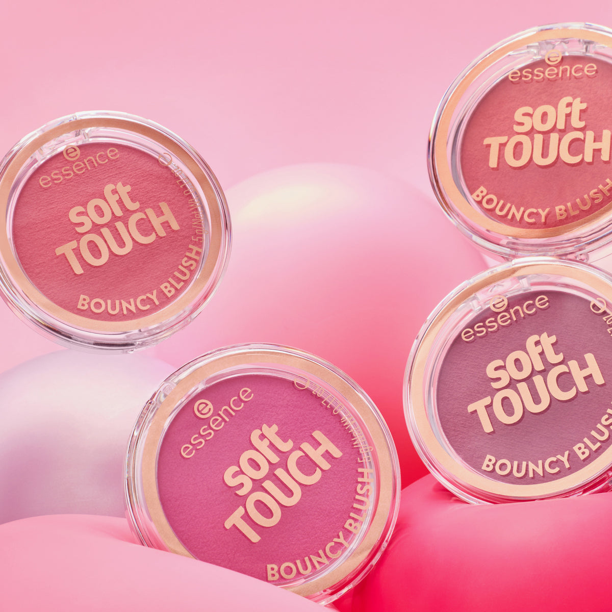 Vier Essence soft TOUCH BOUNCY BLUSH compacts in Rosa- und Lila-Tönen sind auf einem rosa Hintergrund abgebildet.