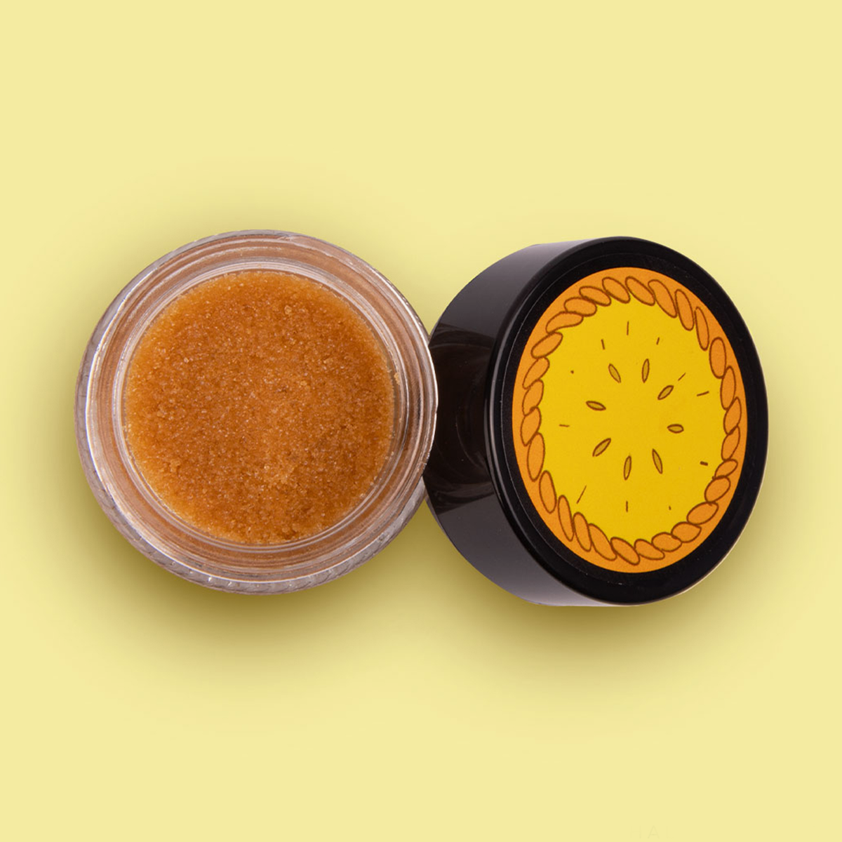 Vogelperspektive des Tiegels mit oranger Adventure Time Tree Trunks Lip Scrub und schwarzem Deckel mit Pie-Aufdruck.