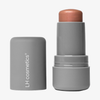 Eine graue Tube LH Cosmetics Artistick Highlighter mit abgenommener Kappe, die daneben liegt.