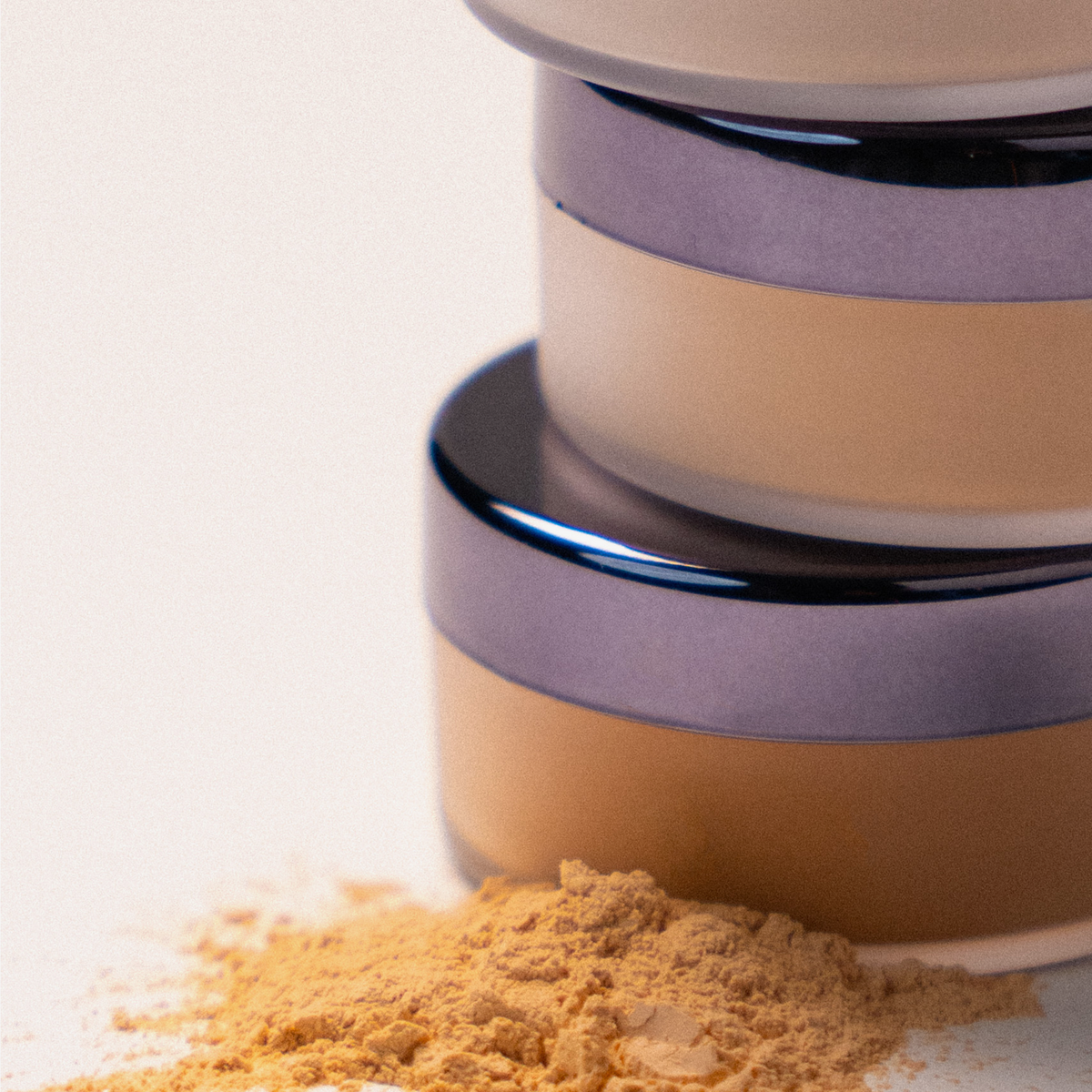 Drei gestapelte LH Cosmetics Infinity Filter Puder mit losem Puder davor auf einer weißen Fläche.