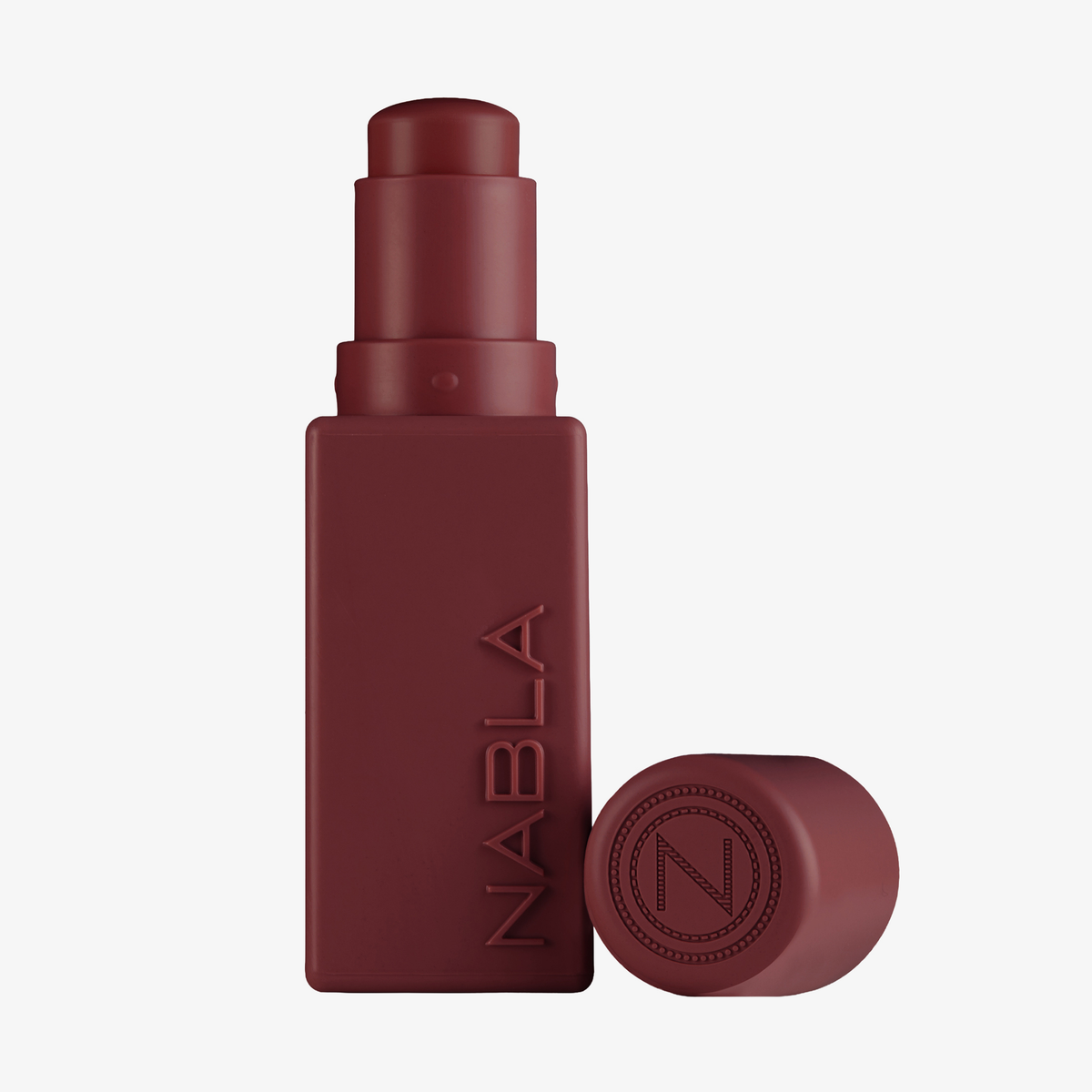Ein dunkelroter „Art Of Skin Blush Stick“ Gelso von NABLA Cosmetics mit einer dazu passenden Kappe daneben.