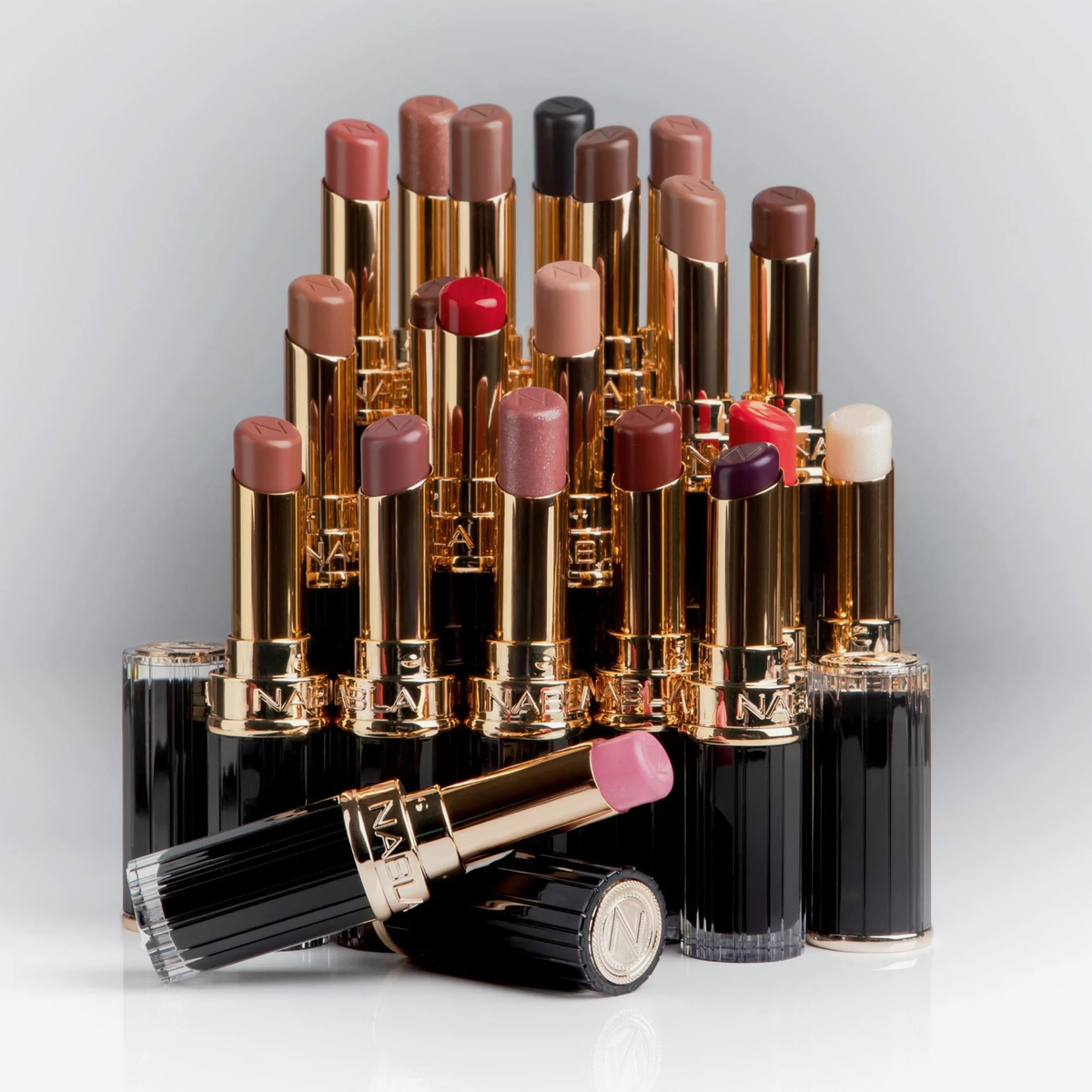 NABLA Cosmetics Beyond Jelly Lipstick Perlglanztuben in Gold und Schwarz, in Reihen angeordnet, eine vorne offen.