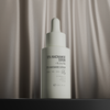 Eine weiße NERDS.-Flasche mit der Aufschrift "12% Niacinamide + 1% Zinc PCA Serum" steht vor dem Hintergrund eines beigefarbenen Seidenvorhangs.