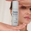 Eine Frau hält eine Flasche „NERDS. Barrier Prep & Comfort Mist“ vor ihr Gesicht und zeigt das Etikett.