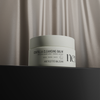Ein Tiegel mit NERDS. Centella Cleansing Balm ruht auf einer dunklen Fläche mit einem beigen, seidigen Vorhang im Hintergrund.