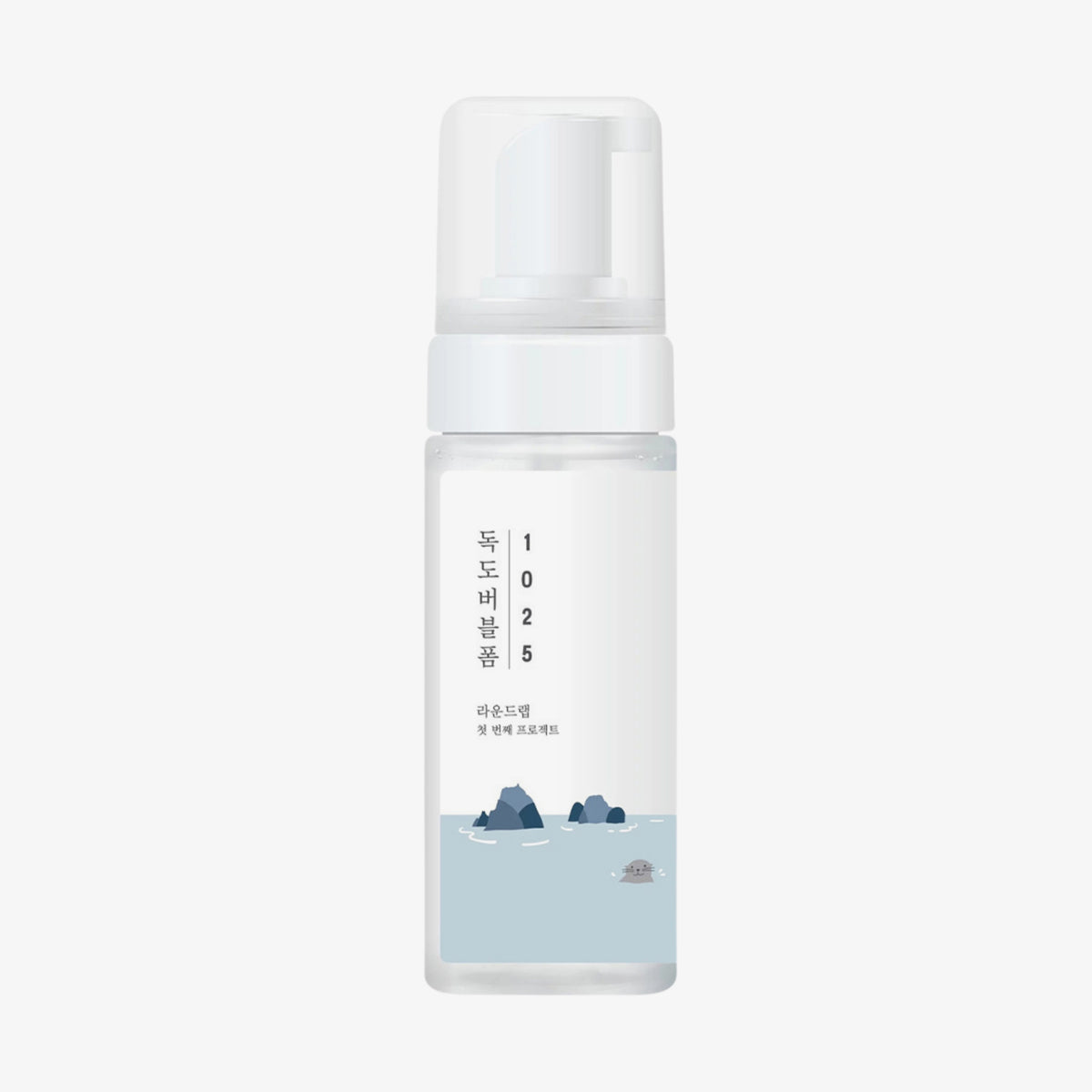 1025 Dokdo Bubble Foam von ROUND LAB kommt in einer durchsichtigen Flasche mit einer weißen Pumpe und einem Etikett mit blauem Wasser, Felsen und koreanischem Text.