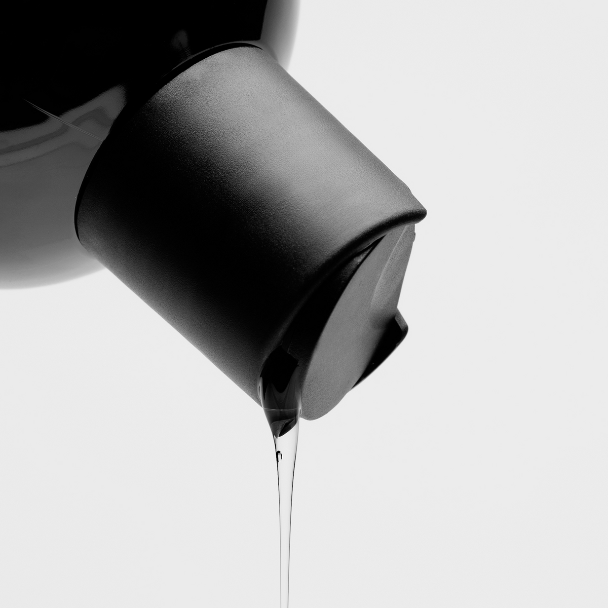 Nahaufnahme eines schwarzen Shampoo-Spenders, aus dem transparente Flüssigkeit tropft, vor hellem Hintergrund.