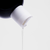 Bio-Pilixin® Shampoo+Women von Scandinavian Biolabs: Die klare Flüssigkeit fließt aus einer schwarzen Flasche mit weißem Deckel, die vor einem schlichten weißen Hintergrund präsentiert wird.