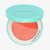 Eine türkisfarbene Puderdose mit offenem Deckel gibt den Blick frei auf die leuchtend korallenfarbene „Air Blush Cream“ sowie das SWEED-Logo auf dem Deckel und dem Rand.