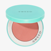 Eine türkisfarbene „Air Blush Cream“-Dose von SWEED mit pfirsichfarbenem Rouge im Inneren, auf deren Deckel und Rand die Aufschrift „SWEED“ zu sehen ist.