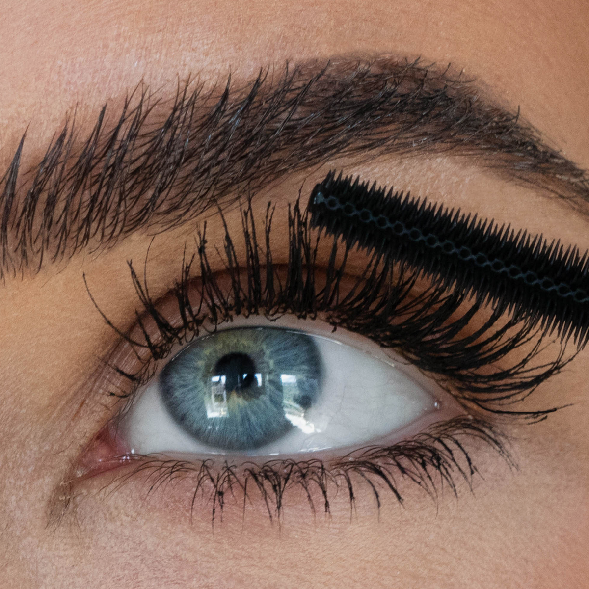 Eine Nahaufnahme, wie die „Cloud Mascara“ von SWEED mit einem schwarzen Applikator auf lange, dunkle Wimpern in der Nähe eines blauen Auges aufgetragen wird.