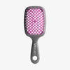 Die UNbrush Detangling Hair Brush hat einen grauen Griff mit dem UNbrush"-Schriftzug, ein pinkfarbenes Kissen und breite Borsten zum leichten Entwirren.