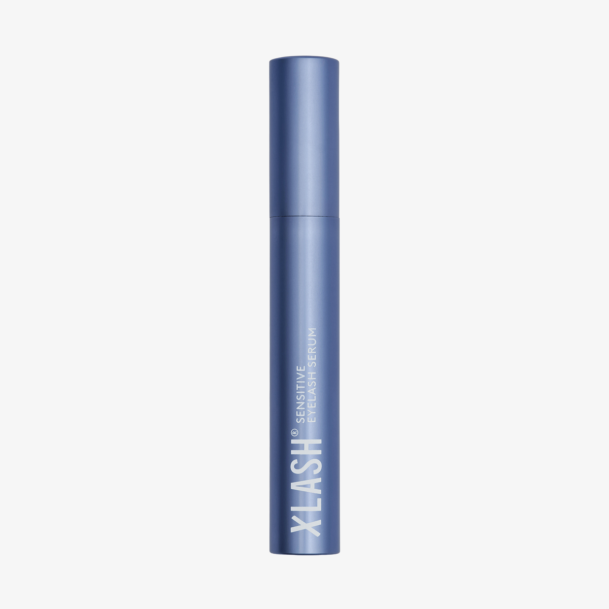 Eine blaue Tube des XLASH Xlash Sensitive Wimpernseren steht aufrecht auf einem weißen Hintergrund.