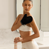 In einem Badezimmer trägt eine Frau mit einem schwarzen Handschuh „Bali Body Self Tanning Mousse Light to Medium“ auf ihren Arm auf.