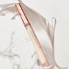 Catrice Colour Cushion Juicy Lip Oil in elegantem Nude-Design mit roségoldenem Deckel, vor einem weißen Hintergrund mit schwungvollen Strukturen.