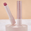Catrice Diamond Glaze Gloss Stick in einem schimmernden Beerenton, geöffnet mit sichtbarer Produktspitze, neben geschlossenem Stick auf hellem Podest.