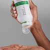 Jemand gießt Philip Kingsley Flaky/Itchy Scalp Hydrating Curl Shampoo aus einer weißen Flasche in seine Handfläche, sodass sich Schaum auf seiner Hand bildet.