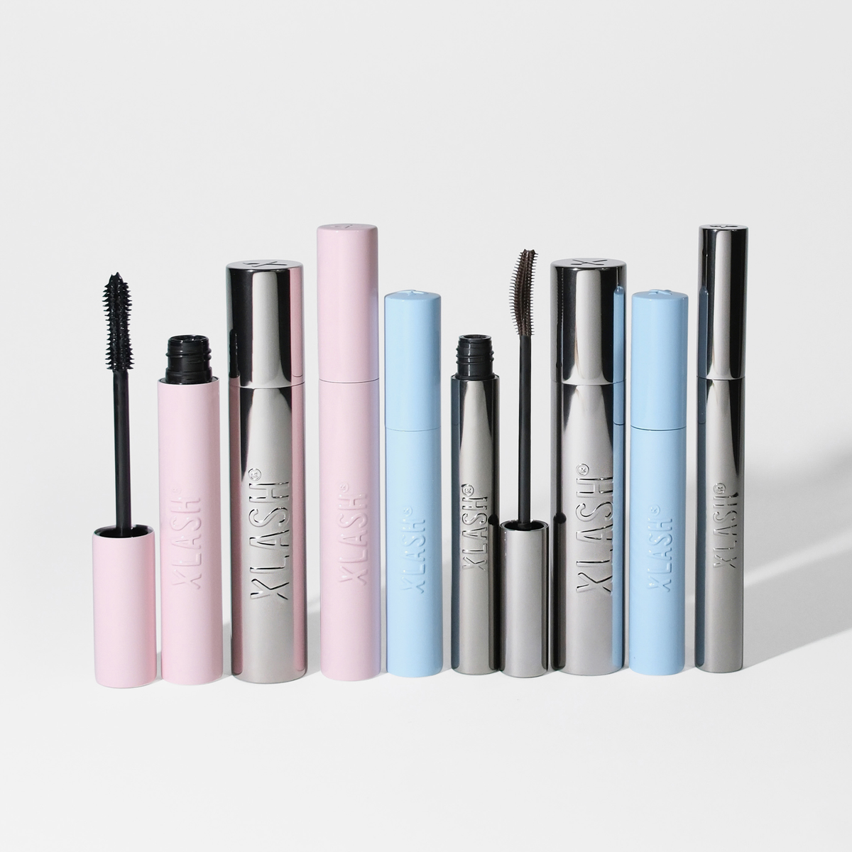 Acht Tuben der XLASH Lash Hero Mascara in den Farben Rosa, Silber und Blau stehen aufrecht auf einem weißen Hintergrund.