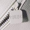 Nahaufnahme der PURISH-Reisetasche – Cremefarben, mit einem weißen Reißverschluss und einem quadratischen Schieber mit der Aufschrift „PURISH“ auf strukturiertem Stoff.