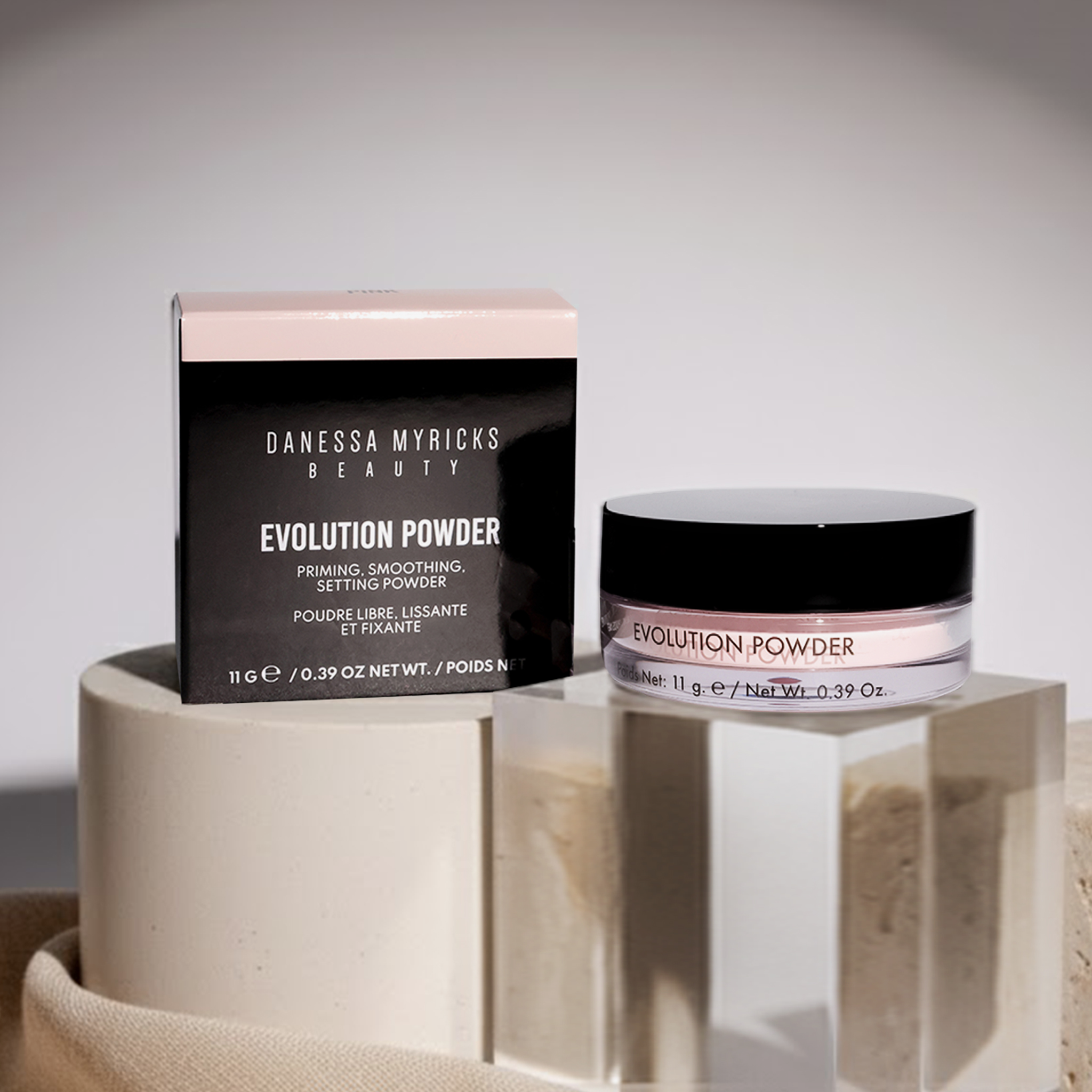 Evolution Powder Pink von Danessa Myricks Beauty mit Schachtel, ausgestellt auf geometrischen Steinplattformen unter sanfter Beleuchtung.
