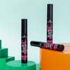 Drei Tuben der Essence lash WITHOUT LIMITS TUBING Extreme Lengthening & Volume Mascara 04 auf leuchtend grünen und orangefarbenen Podesten.