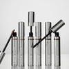 Sechs silberne XLASH Brow Booster-Tuben mit Applikatorstäbchen, von denen einige geöffnet abgebildet sind, zusammen mit Pinseln für getöntes Augenbrauengel.