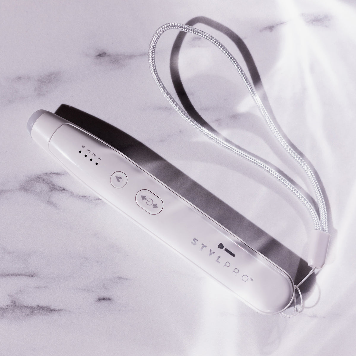 Der STYLPRO Bite Pen, ein weißes elektronisches Gerät mit einer Handschlaufe, wird auf einer von sanftem Sonnenlicht beleuchteten Marmorfläche präsentiert.