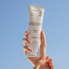 Eine Hand hält eine Tube „Transparent Lab Invisible Sunscreen SPF50+“ vor einen strahlend blauen Himmel.