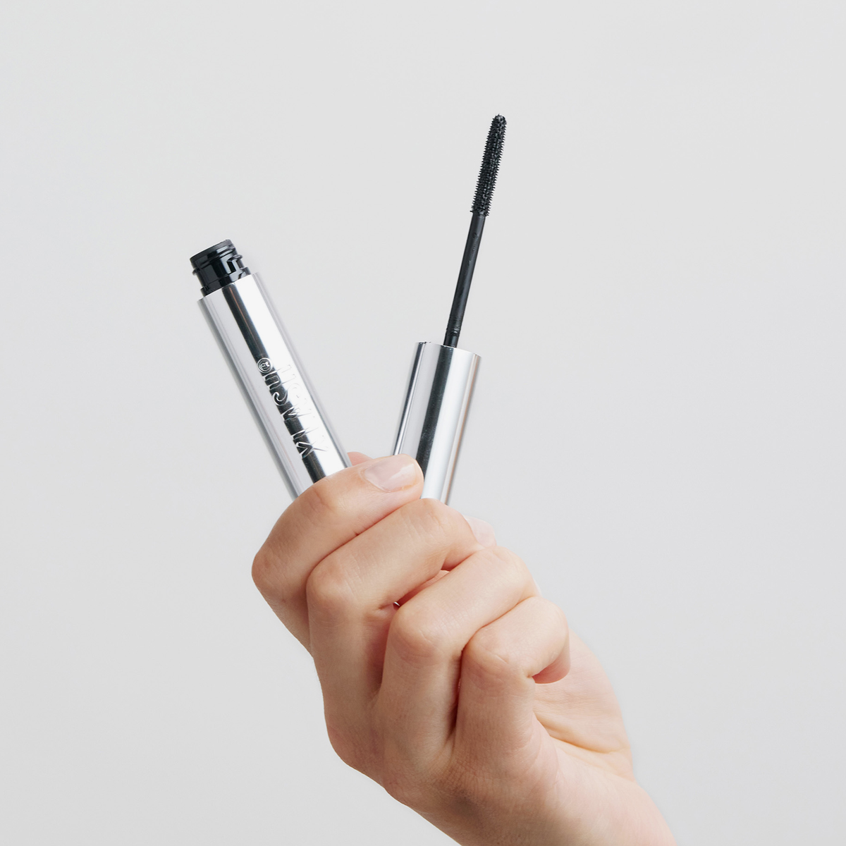 Eine Hand, die eine geöffnete Tube XLASH Lash Booster hält, wobei der Applikator herausgezogen ist.