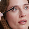 Eine Frau trägt die XLASH Lash Hero Mascara mit einem Applikator mit rosa Griff auf ihre oberen Wimpern auf.