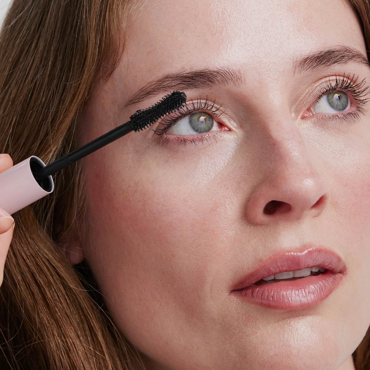 Eine Frau trägt die XLASH Lash Hero Mascara mit einem Applikator mit rosa Griff auf ihre oberen Wimpern auf.