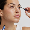 Eine Frau trägt das Xlash Eyelash Serum mit einem blauen Applikator auf ihre oberen Wimpern auf.