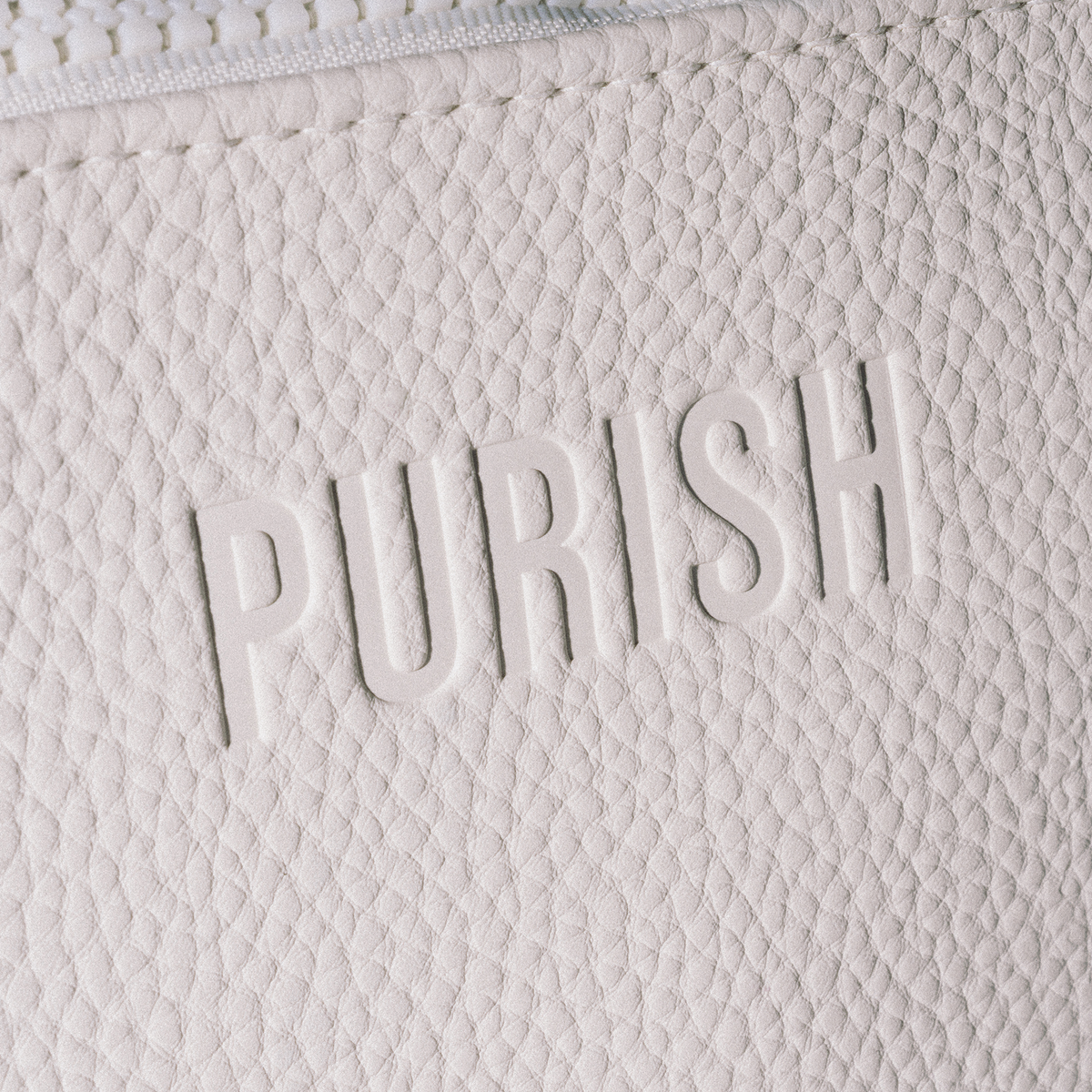 Die Nahaufnahme der PURISH-Reisetasche – Creme zeigt das Wort „PURISH“, das auf der strukturierten weißen Oberfläche eingeprägt ist.