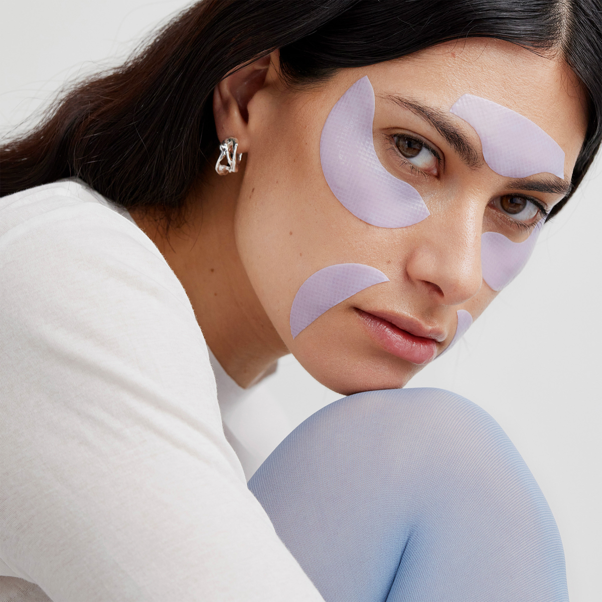 Eine Person, die hellviolette Longevity Multi-Zone Gels-Hautpflege-Pflaster unter den Augen und auf der Stirn trägt.