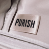 An der cremefarbenen PURISH-Reisetasche ist ein weißes Stoffetikett mit der Aufschrift „PURISH“ in schwarzer Schrift aufgenäht.