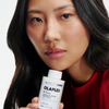 Eine Frau in einem roten Oberteil hält OLAPLEX N°3 PLUS Complete Repair Treatment nahe an ihr Gesicht.