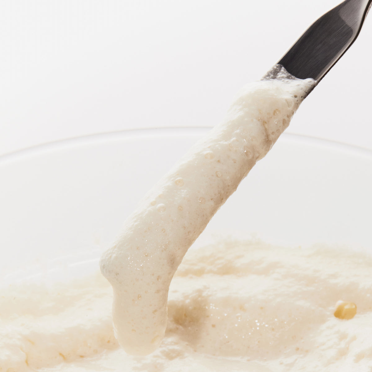 Ein Metallspatel hebt das Rice Enzyme Brightening Cleansing Powder aus seiner Schale.