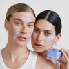 Zwei Frauen tragen hellviolette Longevity Multi-Zone Gels auf ihr Gesicht auf; eine von ihnen hält einen passenden Tiegel mit den Pflastern in der Hand.