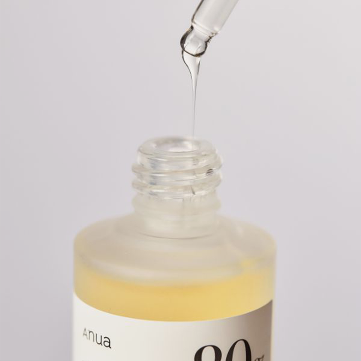 Eine Pipette gibt die „Heartleaf 80 % Soothing Ampoule“ von ANUA in eine offene, mattierte Flasche vor einem hellen Hintergrund ab.